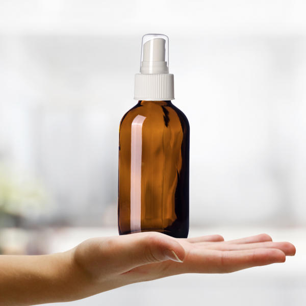 4oz Amber Glass Spray Bottle with White Spray Cap held on palm of hand to show size